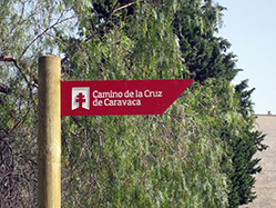 A post with an arrow in a rural area in which the logo and name of the Camino can be seen.